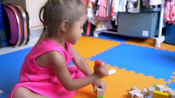 小亚洲可爱的女孩玩立方体, 坐在一个彩色地板上。儿童发展的概念. — 图库视频影像