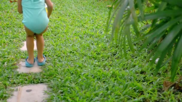 Aziatische meisje in een badpak wandelen langs een kleine pad in de tuin. — Stockvideo