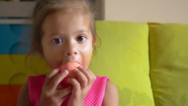 Liten söt asiatisk flicka äter ett äpple som ligger på sängen — Stockvideo