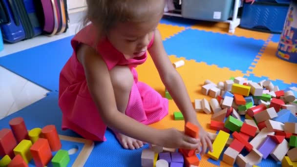 Kis-ázsiai aranyos lány játék kocka, egy színes padlón ül. A gyermek fejlődési koncepció. — Stock videók