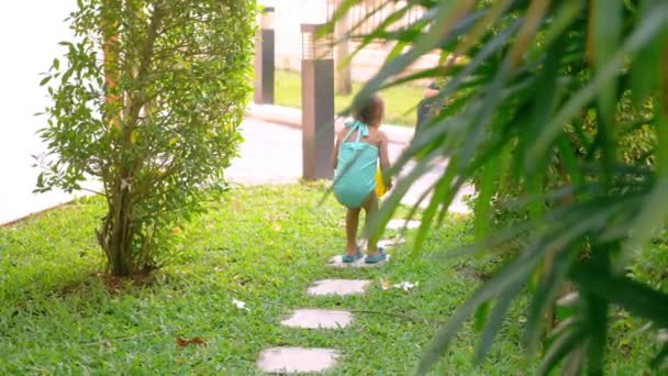 Kleine asiatische Mädchen in einem Badeanzug zu Fuß auf einem kleinen Pfad in den Garten. — Stockvideo