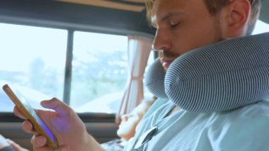 Genç bir adam bir arabada seyahat yastık ile bir akıllı telefon kullanır. Yol seyahat konsepti