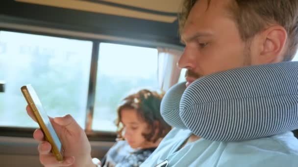 Un joven con una almohada de viaje en un coche utiliza un teléfono inteligente. Concepto de viaje por carretera — Vídeos de Stock