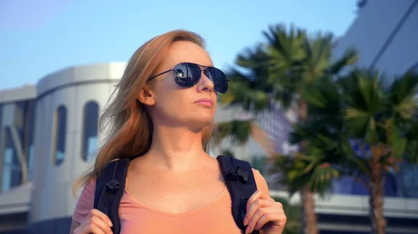 El concepto de turismo. Mujer turista en gafas de sol con una mochila en la espalda va al aeropuerto en el fondo del avión. mujer rubia sonriendo en el aeropuerto —  Fotos de Stock