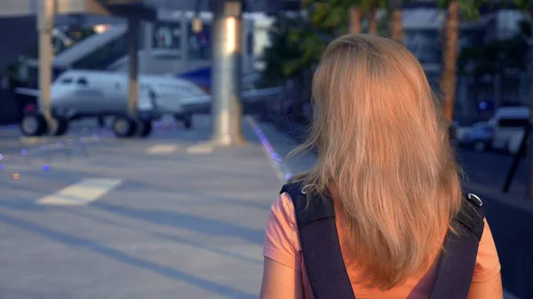 Turizm kavramı. Sırtında bir sırt çantası ile güneş gözlüklü kadın turist uçağın arka plan üzerinde havaalanına gider. havaalanında gülümseyen kadın sarışın — Stok fotoğraf