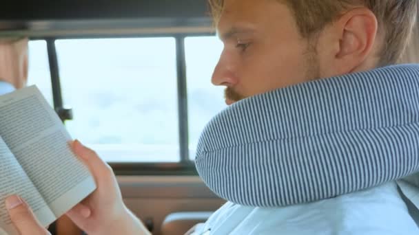 Jovem com travesseiro de viagem no carro lendo um livro. conceito de viagem rodoviária — Vídeo de Stock