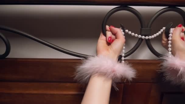 De handen van een vrouw in bont handboeien worden gehouden door een smeedijzeren hoofdeinde. Close-up — Stockvideo