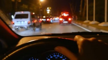 bulanıklık, birinci şahıs görünümü. arabanın direksiyonuna el. bir gece şehir yolunda trafikte sürüş. cam üzerinde yağmur damlaları