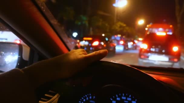 Sfocatura, vista in prima persona. mano sul volante dell'auto. guida nel traffico su una strada notturna della città. gocce di pioggia sul vetro — Video Stock