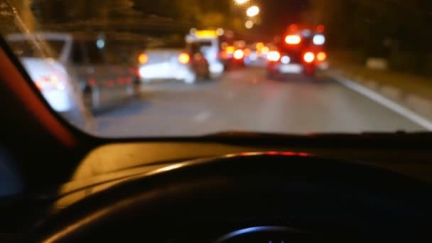 Rozostření, zobrazení první osoby. rukou na volantu vozidla. jízdu v provozu na noční silnici. dešťové kapky na skle — Stock video