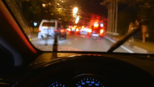 Borrão, vista em primeira pessoa. mão sobre o volante do carro. dirigindo no trânsito em uma estrada noturna da cidade. gotas de chuva no vidro — Vídeo de Stock