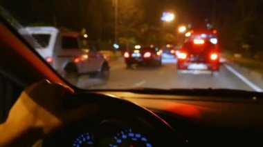 bulanıklık, birinci şahıs görünümü. arabanın direksiyonuna el. bir gece şehir yolunda trafikte sürüş. cam üzerinde yağmur damlaları