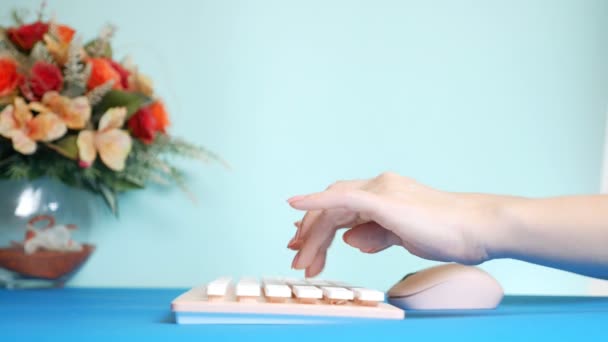 Primer plano. tarjeta de vídeo de saludo con estilo. manos femeninas están escribiendo en un teclado rosa, junto a una flor. sobre un fondo azul . — Vídeo de stock