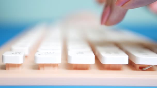 Nahaufnahme. Frauenhände tippen auf einer rosafarbenen Tastatur auf blauem Hintergrund. — Stockvideo