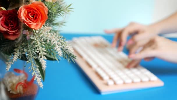 Närbild. snygg hälsning grafikkort. kvinnliga händer skriver på ett rosa tangentbord, bredvid en blomma. på en blå bakgrund. — Stockvideo
