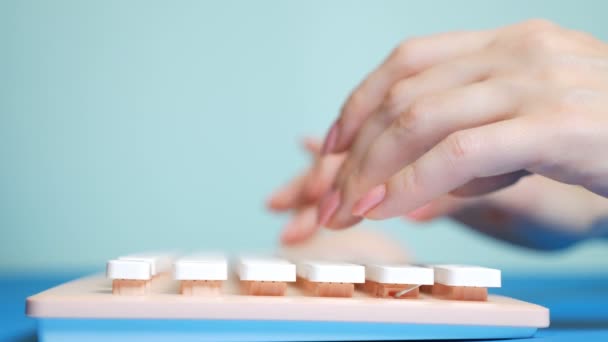 Primer plano. Las manos femeninas están escribiendo en un teclado rosa, sobre un fondo azul . — Vídeos de Stock