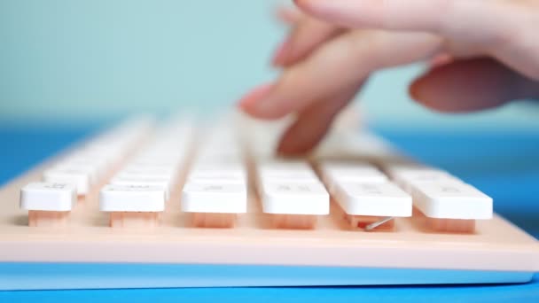 Primer plano. Las manos femeninas están escribiendo en un teclado rosa, sobre un fondo azul . — Vídeos de Stock