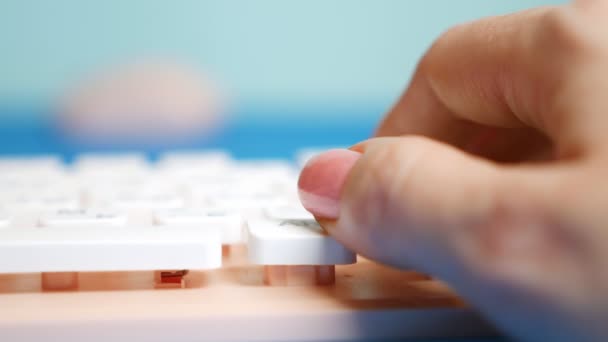 Primer plano. Las manos femeninas están escribiendo en un teclado rosa, sobre un fondo azul . — Vídeos de Stock