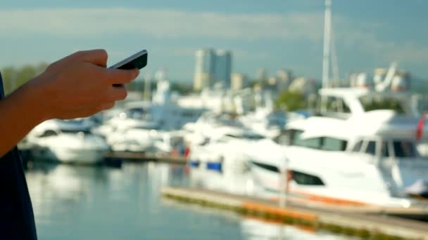 Männliche Hände halten Smartphone auf verschwommenem Hintergrund des Hafens mit Yachten — Stockvideo