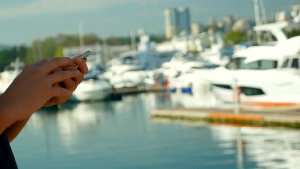 Мужчины держат в руках смартфон на размытом фоне порта с яхтами — стоковое видео