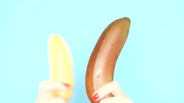 kırmızı tırnaklı kadın elleri mavi bir arka plan üzerinde kırmızı bir muz ve sarı bir muz tutuyor