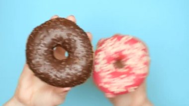 Çikolatalı çörek ve çilekli çörek arasında konsept seçimi. kırmızı oje ile kadın elleri mavi bir arka plan üzerinde pembe ve kahverengi donut tutun