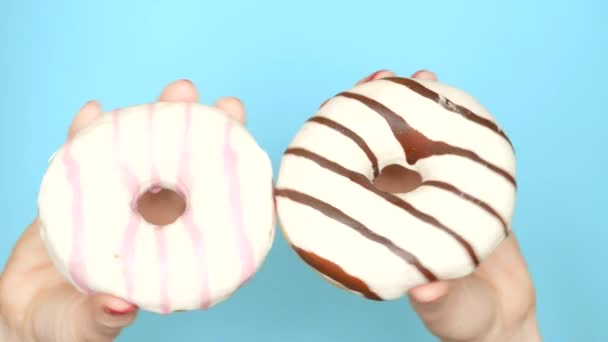 Concepto de elección entre donut de chocolate y donut de fresa. manos femeninas con esmalte de uñas rojo sostienen rosado y rosado rosquilla sobre un fondo azul — Vídeo de stock