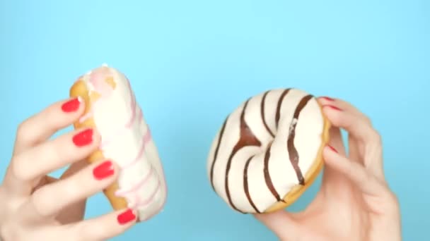 Concepto de elección entre donut de chocolate y donut de fresa. manos femeninas con esmalte de uñas rojo sostienen rosado y rosado rosquilla sobre un fondo azul — Vídeo de stock