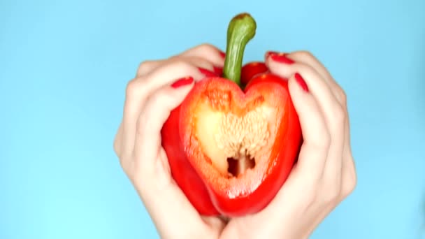 Γυναικεία χέρια με κόκκινο μανικιούρ κρατούν κόκκινο γλυκό πιπέρι στο χέρι με τη μορφή της καρδιάς σε μπλε φόντο — Αρχείο Βίντεο