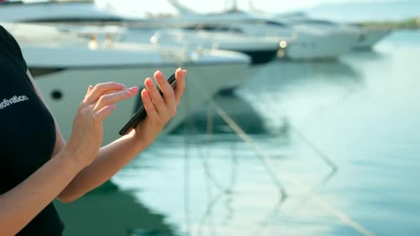 Mano femenina sostiene teléfono inteligente sobre fondo borroso del puerto con yates — Vídeos de Stock