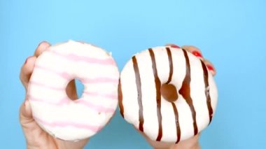 Çikolatalı çörek ve çilekli çörek arasında konsept seçimi. kırmızı oje ile kadın elleri mavi bir arka plan üzerinde pembe ve kahverengi donut tutun