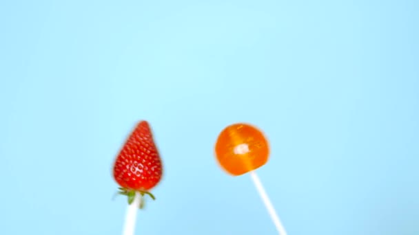 Concepto de comida saludable y poco saludable. fresa contra caramelos sobre un fondo azul brillante — Vídeos de Stock