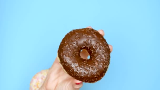 Concept keuze tussen chocolade donut en aardbei donut. vrouwelijke handen met rode nagellak houden roze en bruine donut op een blauwe achtergrond — Stockvideo