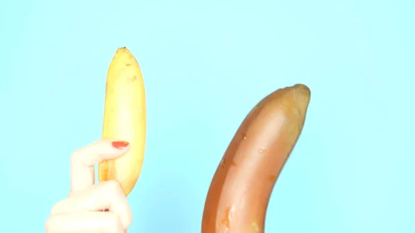 Mains féminines avec des ongles rouges tiennent une banane rouge et une banane jaune sur un fond bleu — Photo