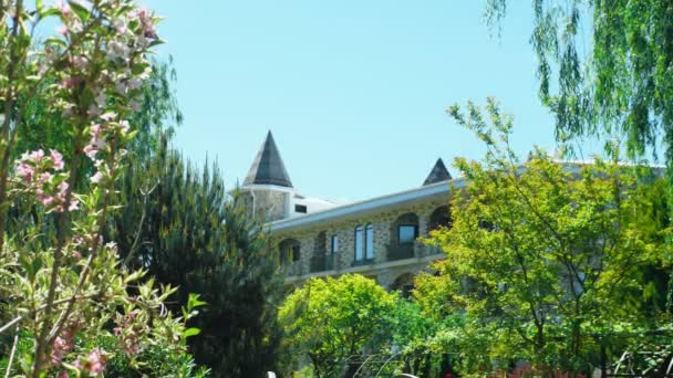 Luxurious hotel in Victorian style, immersed in beautiful trees and bushes. roofs with spiers on a background of clear blue sky — Stock Video