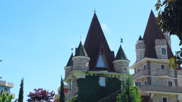 Luxurious hotel in Victorian style, immersed in beautiful trees and bushes. roofs with spiers on a background of clear blue sky — Stock Video