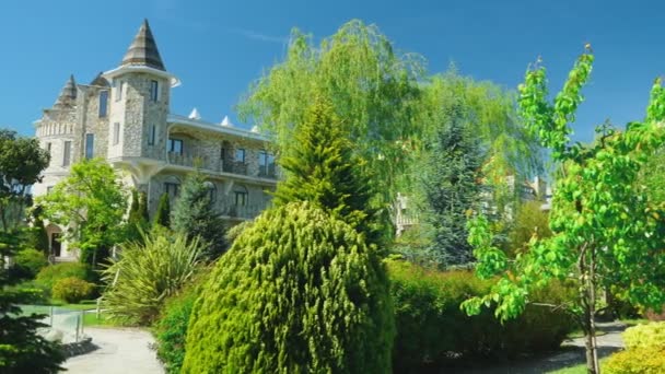 Luxurious hotel in Victorian style, immersed in beautiful trees and bushes. roofs with spiers on a background of clear blue sky — Stock Video