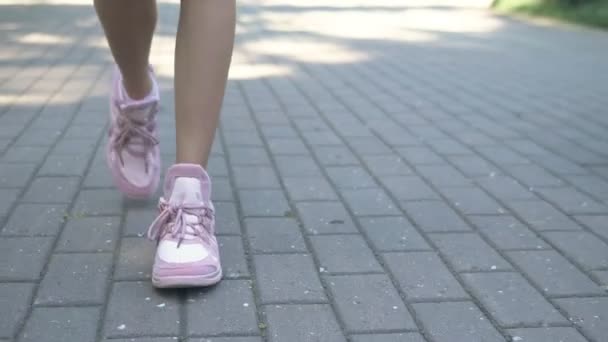 Nahaufnahme. Frauenbeine in stylischen rosa Turnschuhen. Mädchen läuft auf der Straße mit Pflaster. natürliches sonniges Tageslicht — Stockvideo