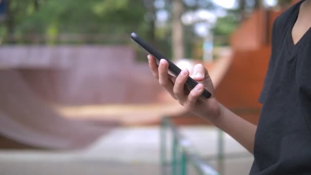 Teen boy sam za pomocą telefonu komórkowego na tle skate parku. podczas gdy inne dzieci aktywnie się odprężają. Uzależnienie od smartfonów — Wideo stockowe