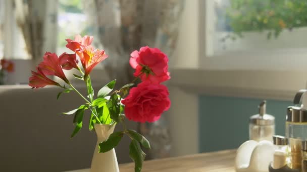 Close-up. Cute bouquet of red roses and freesia in a vase on a table on a sunny summer day in a cafe — Stock Video