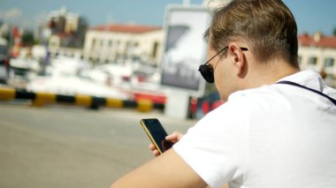 Yatlar ile liman bulanık arka plan üzerinde akıllı telefon tutan adam