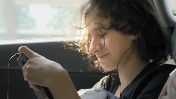 happy teen boy in headphones uses phone in car