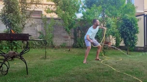 Speelse jonge man in de achtertuin gieter gras tijdens een picknick en dansen — Stockvideo