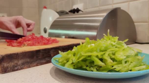Um close-up de um prato de páprica verde finamente picada. contra o pano de fundo das mãos femininas cortando tomates — Vídeo de Stock