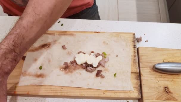 Primer plano. Manos de hombre están preparando shawarma. El proceso de cocinar delicioso shawarma con carne, verduras y crema agria. sobre una tabla de cortar de madera — Vídeos de Stock