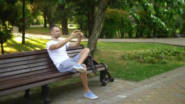 tam çekim. Bir adam blogcu bir park bankında otururken bir akıllı telefon kullanır. Birisiyle görüntülü görüşmesi var.