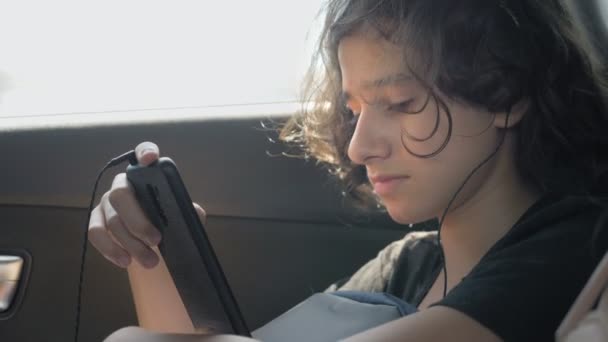 Szczęśliwy nastolatek chłopiec w słuchawkach używa telefonu w samochodzie — Wideo stockowe