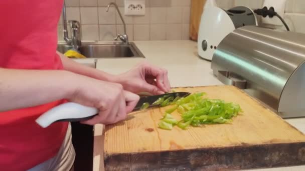 Крупним планом. жінка вирізає зелену паприку на дерев'яній дошці на домашній кухні — стокове відео