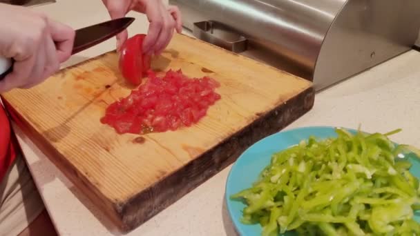 Un primer plano de un plato de pimentón verde finamente picado. contra el fondo de manos femeninas rebanando tomates — Vídeo de stock