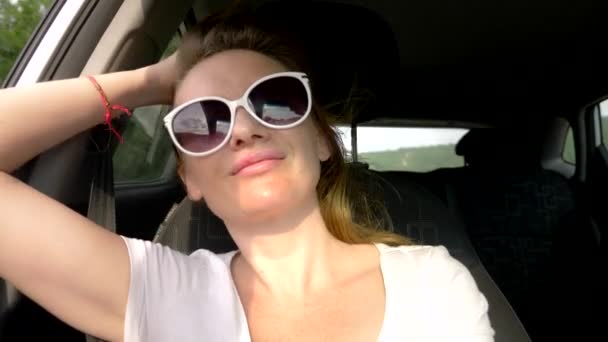 Mujer joven feliz en gafas de sol mira a la ventana abierta del coche, y su pelo largo es excitado por el viento. auto viaje y aventura concepto — Vídeos de Stock